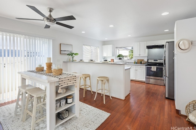 kitchen with kitchen peninsula, appliances with stainless steel finishes, a kitchen breakfast bar, dark hardwood / wood-style floors, and white cabinetry