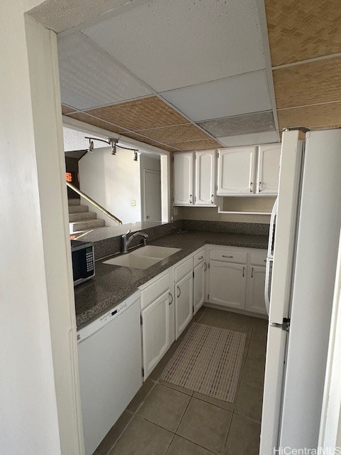 kitchen featuring sink, white appliances, a paneled ceiling, white cabinets, and dark tile patterned flooring