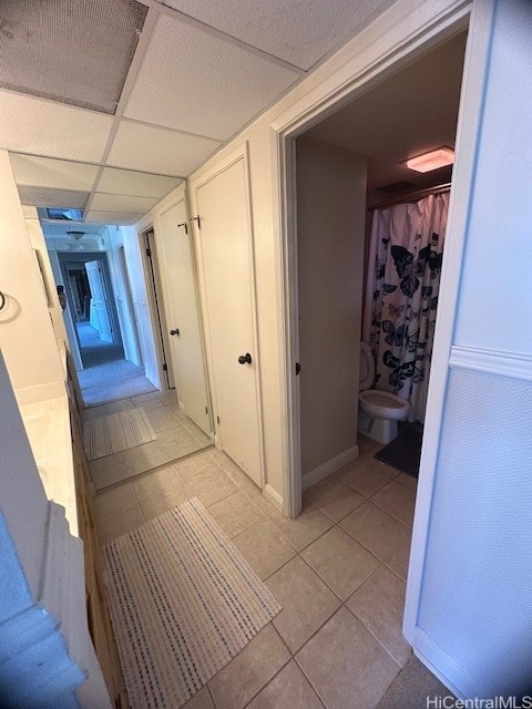 hall featuring a paneled ceiling and light tile patterned floors