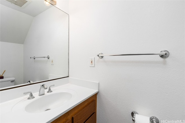 bathroom featuring vanity, toilet, and vaulted ceiling