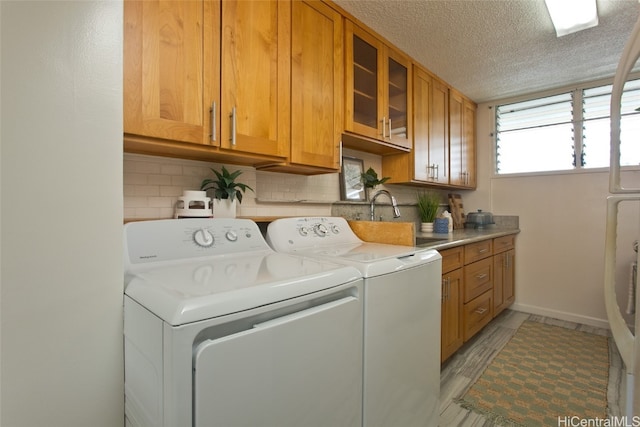 laundry room with cabinets, sink, a textured ceiling, light hardwood / wood-style floors, and washing machine and clothes dryer