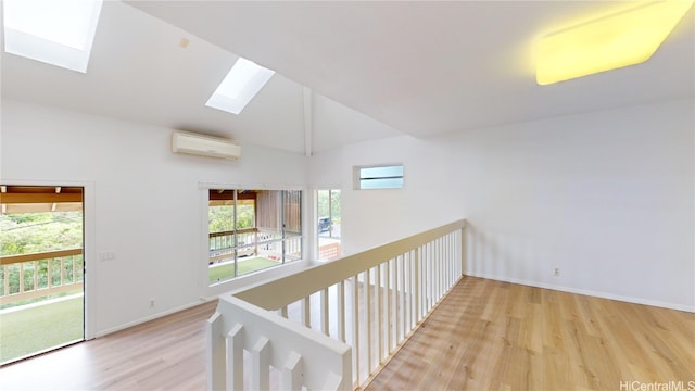 hallway with a wall unit AC, a skylight, high vaulted ceiling, and light hardwood / wood-style floors