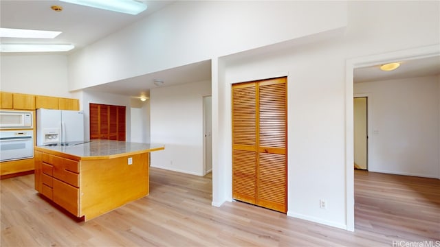 kitchen featuring a skylight, white appliances, light hardwood / wood-style flooring, a high ceiling, and a kitchen island