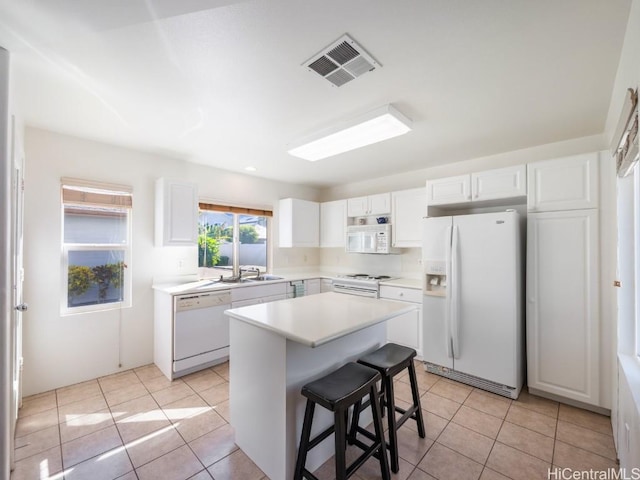 kitchen featuring light tile patterned floors, a kitchen island, a kitchen breakfast bar, white appliances, and white cabinets