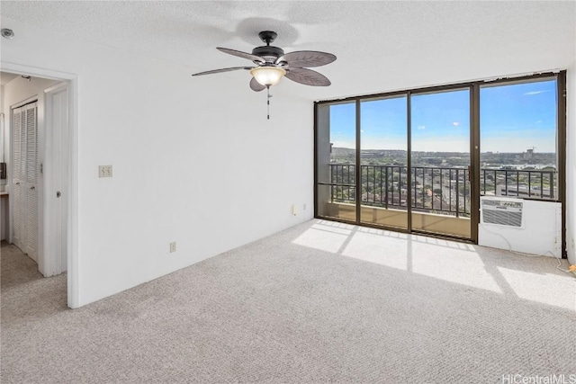 carpeted empty room with a wall mounted air conditioner, ceiling fan, expansive windows, and a textured ceiling