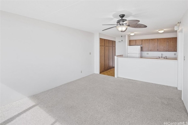 unfurnished living room featuring light carpet, ceiling fan, and sink