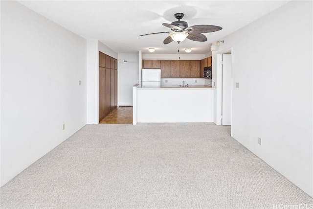 unfurnished living room with light colored carpet, ceiling fan, and sink