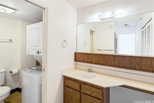 bathroom with parquet flooring, a textured ceiling, vanity, stacked washer and dryer, and toilet