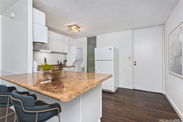 kitchen featuring white refrigerator, stacked washer and dryer, dark hardwood / wood-style floors, a textured ceiling, and white cabinetry