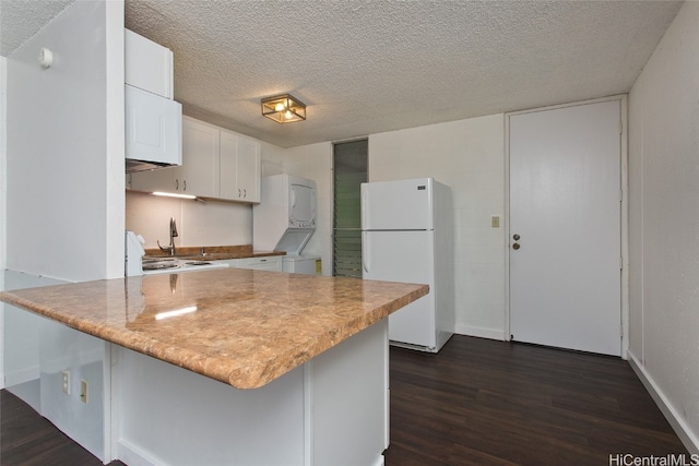 kitchen with stacked washing maching and dryer, kitchen peninsula, white fridge, and white cabinetry