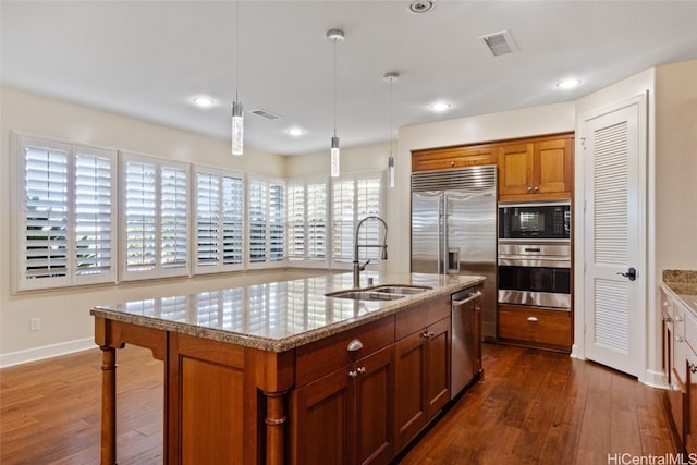 kitchen with sink, dark hardwood / wood-style floors, pendant lighting, a center island with sink, and appliances with stainless steel finishes