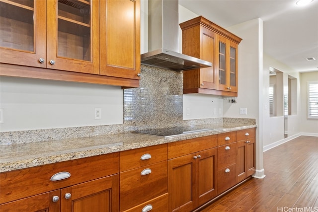 kitchen with backsplash, light stone counters, wall chimney exhaust hood, cooktop, and dark wood-type flooring