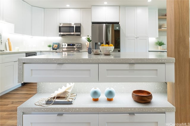 kitchen with light stone countertops, white cabinetry, light hardwood / wood-style flooring, and stainless steel appliances