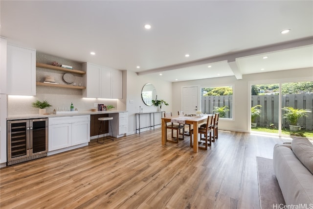 kitchen featuring beverage cooler, tasteful backsplash, light hardwood / wood-style flooring, beamed ceiling, and white cabinets