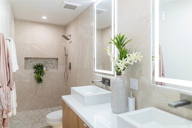 bathroom featuring vanity, toilet, tile walls, and a tile shower