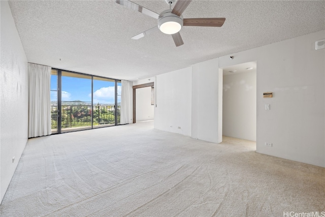 unfurnished room with light carpet, ceiling fan, a textured ceiling, and a wall of windows