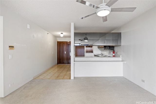 kitchen with kitchen peninsula, refrigerator, light colored carpet, and a textured ceiling