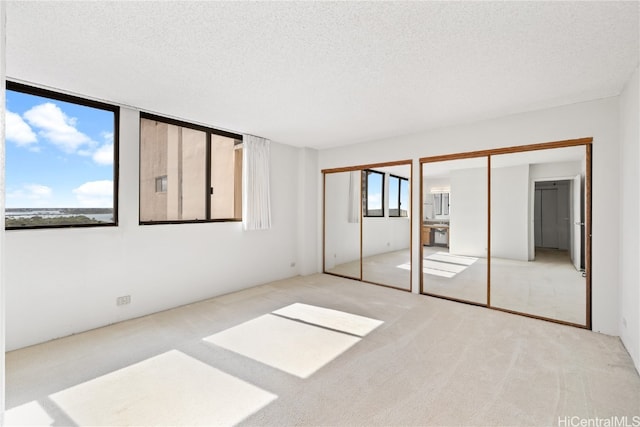 unfurnished bedroom with a textured ceiling, light carpet, and two closets