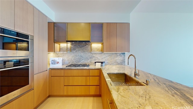 kitchen featuring backsplash, sink, wall chimney exhaust hood, light stone countertops, and appliances with stainless steel finishes