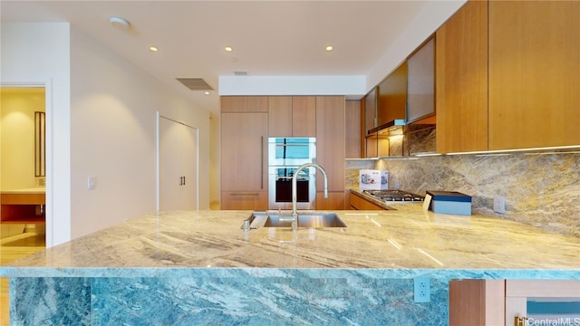 kitchen featuring decorative backsplash, light stone counters, stainless steel gas cooktop, and sink