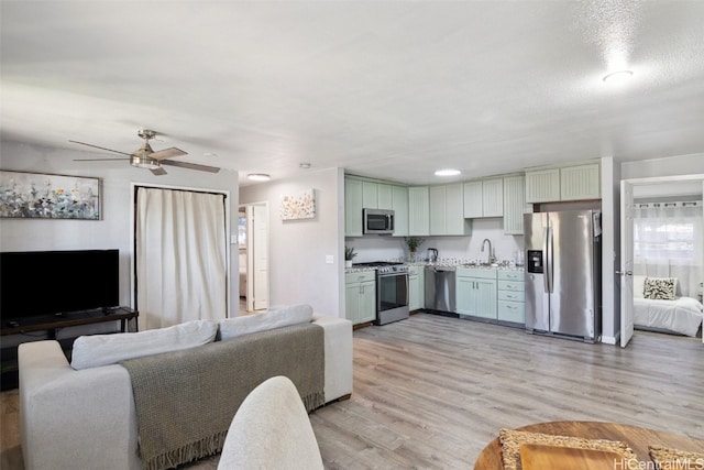 living room with ceiling fan, sink, a textured ceiling, and light wood-type flooring