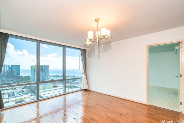 empty room featuring a wall of windows, wood-type flooring, a water view, and an inviting chandelier