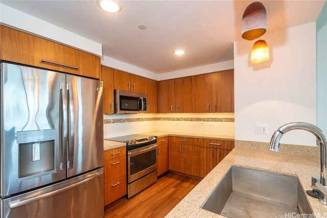 kitchen with light stone countertops, sink, backsplash, appliances with stainless steel finishes, and hardwood / wood-style flooring