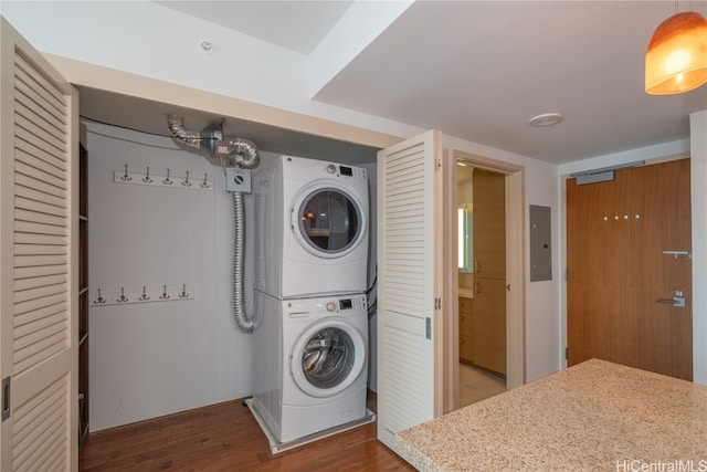 laundry area with electric panel, stacked washer and dryer, and hardwood / wood-style flooring