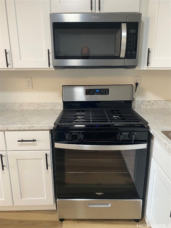 kitchen with white cabinets, appliances with stainless steel finishes, light wood-type flooring, and light stone counters