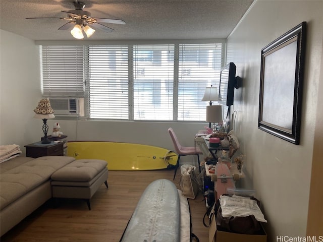 living room featuring ceiling fan, cooling unit, wood-type flooring, and a textured ceiling