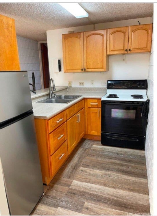 kitchen featuring sink, white electric range oven, light hardwood / wood-style flooring, stainless steel fridge, and a textured ceiling