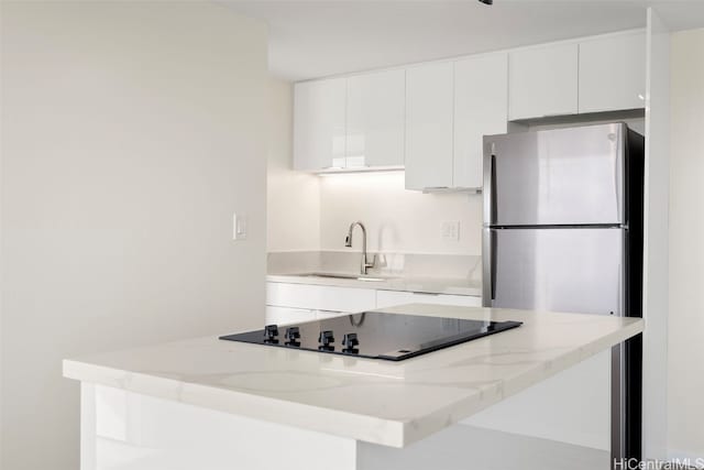 kitchen featuring white cabinetry, sink, light stone countertops, stainless steel fridge, and black electric cooktop