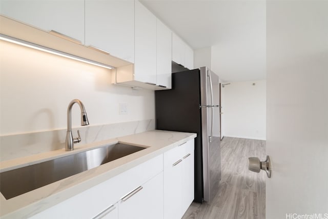 kitchen with sink, light stone countertops, light wood-type flooring, white cabinetry, and stainless steel refrigerator