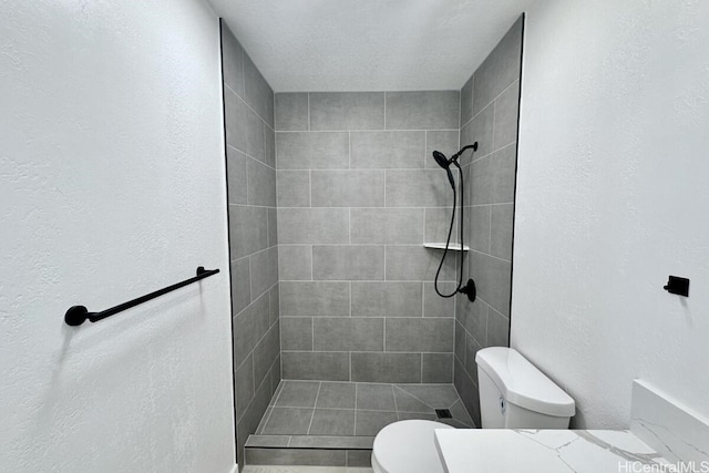 bathroom featuring toilet, a tile shower, and a textured ceiling