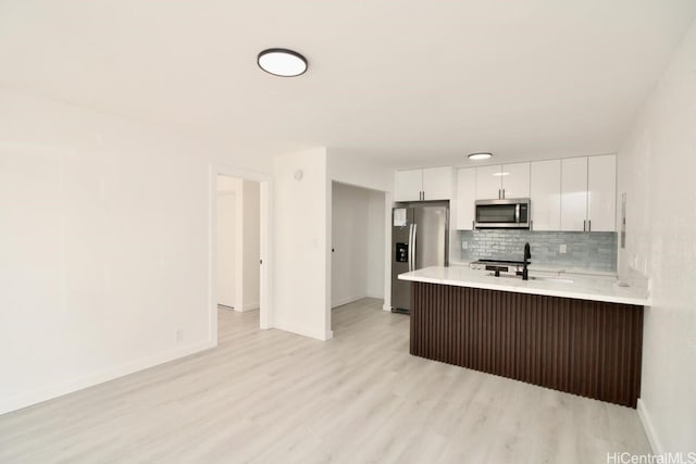 kitchen featuring decorative backsplash, stainless steel appliances, sink, white cabinets, and light hardwood / wood-style floors