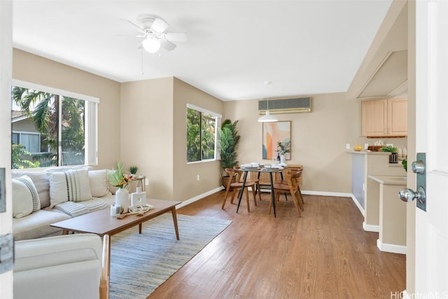 living room with light wood finished floors, a wall mounted air conditioner, a ceiling fan, and baseboards