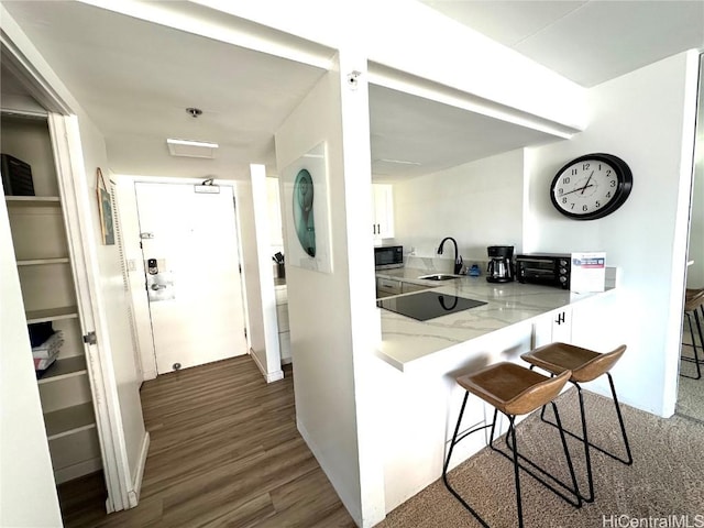 kitchen with sink, white cabinetry, black electric cooktop, a kitchen breakfast bar, and kitchen peninsula