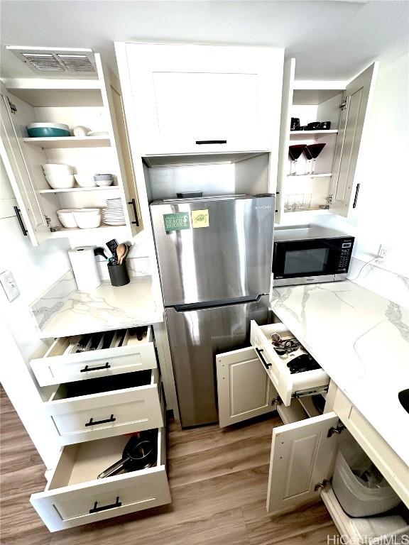 kitchen featuring appliances with stainless steel finishes, hardwood / wood-style floors, white cabinets, and light stone counters