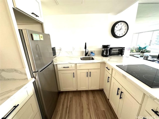 kitchen with sink, stainless steel refrigerator, dark hardwood / wood-style floors, light stone countertops, and black electric cooktop