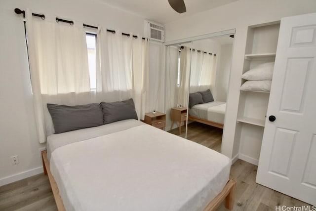 bedroom featuring a wall mounted AC, ceiling fan, a closet, and wood-type flooring