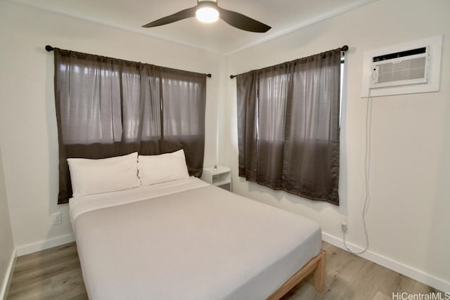 bedroom featuring light hardwood / wood-style floors, a wall unit AC, and ceiling fan