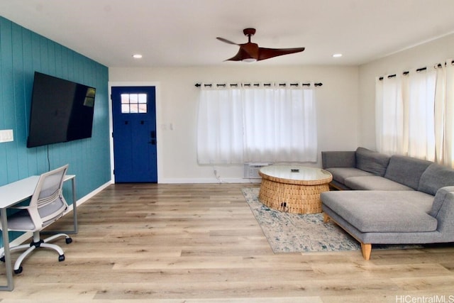 living room with a wall mounted AC, ceiling fan, and light wood-type flooring