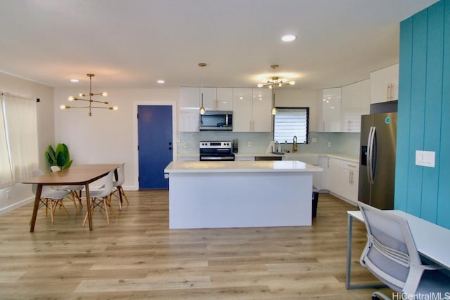 kitchen with light wood-type flooring, tasteful backsplash, stainless steel appliances, decorative light fixtures, and white cabinets