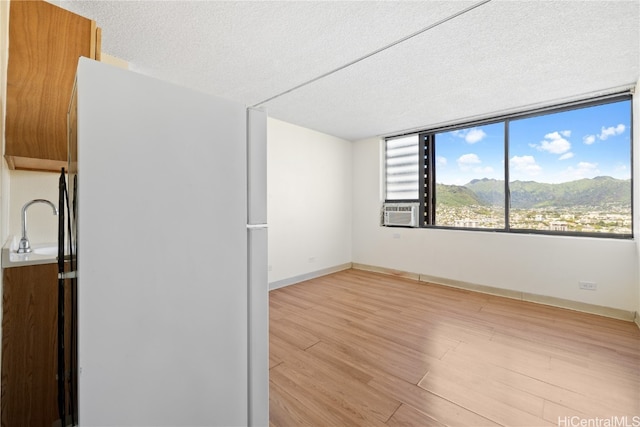 spare room featuring a mountain view, cooling unit, a textured ceiling, and light hardwood / wood-style flooring