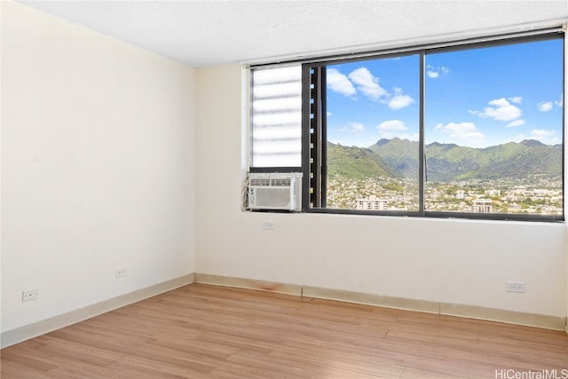 spare room with a mountain view, a textured ceiling, light wood-type flooring, and cooling unit