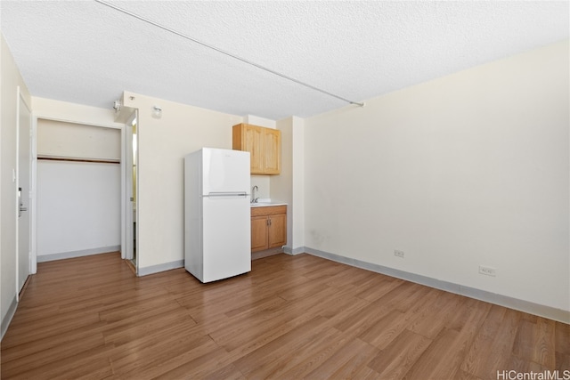 unfurnished bedroom with light wood-type flooring, a textured ceiling, white refrigerator, and sink