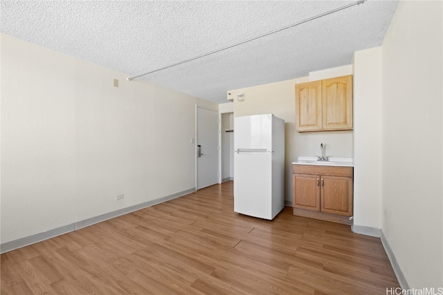 kitchen featuring white refrigerator, sink, a textured ceiling, and light hardwood / wood-style flooring