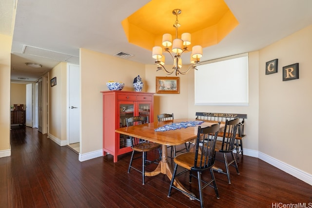 dining room with a tray ceiling, dark hardwood / wood-style floors, and an inviting chandelier