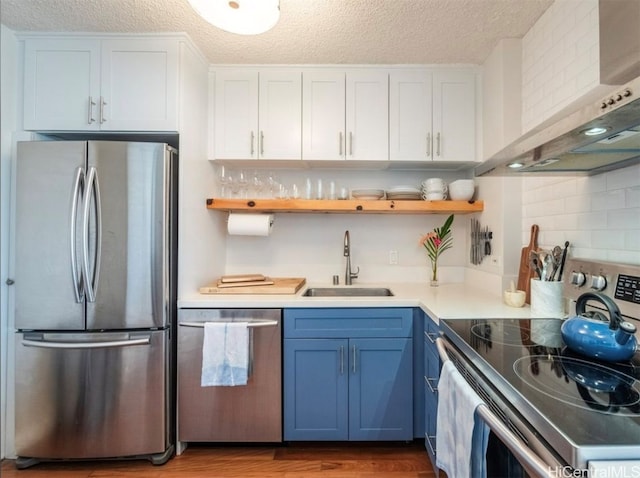 kitchen with wall chimney range hood, sink, blue cabinetry, white cabinetry, and stainless steel appliances