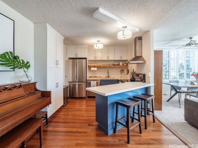 kitchen featuring hardwood / wood-style floors, white cabinets, stainless steel appliances, and wall chimney range hood